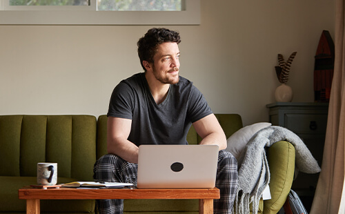 Ein Mann sitzt vor dem Laptop auf der Couch.