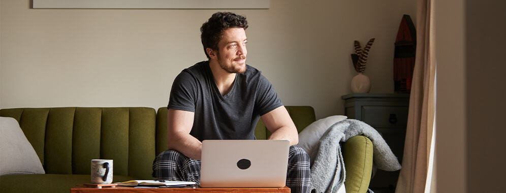 Ein Mann sitzt vor dem Laptop auf der Couch. 
