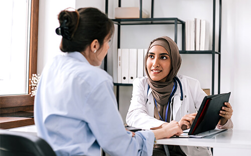 Eine Frau spricht in der Praxis mit einer Ärztin, die etwas auf dem Tablet zeigt.