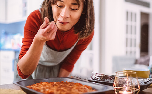 Eine Frau probiert etwas zu essen in der Küche. 