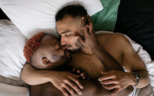 Zwei Männer liegen im Bett und umarmen sich.
