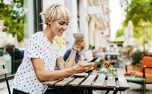 Eine Frau sitzt im Café, trinkt Kaffee und schreibt auf ihrem Handy.