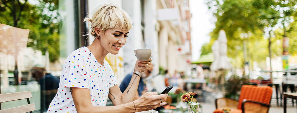 Eine Frau sitzt in einem Café, trinkt Kaffee und schreibt auf ihrem Handy. 