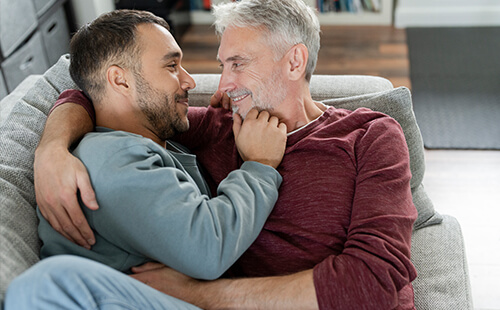 Zwei Männer liegen auf der Couch und umarmen sich.
