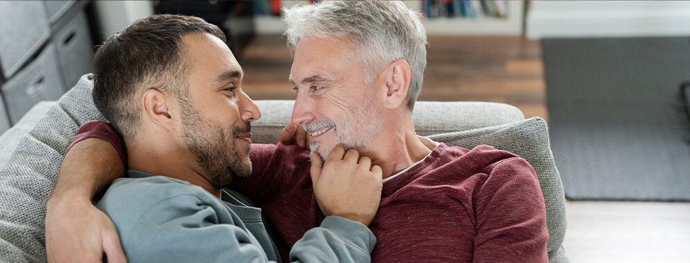 Zwei Männer liegen auf der Couch und umarmen sich.