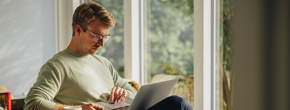 Ein Mann macht etwas an seinem Laptop, den er auf dem Schoß hält. 