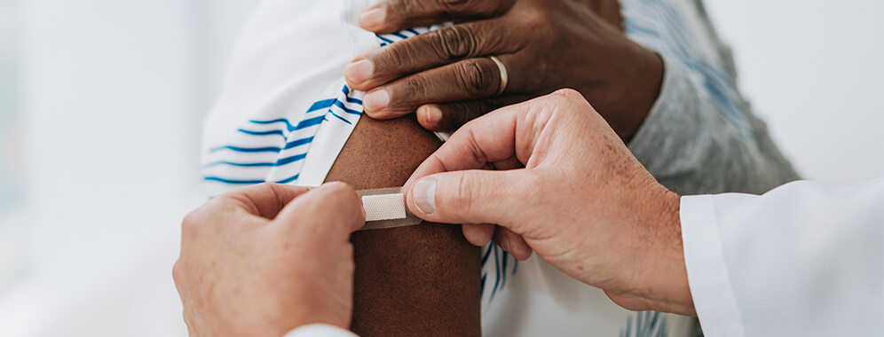 Ein Pflaster wird auf den Oberarm geklebt, wahrscheinlich nach einer Impfung. 