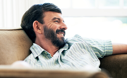 Ein Mann liegt lächelnd auf dem Sofa.