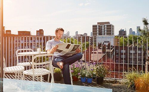 Ein Mann liest auf einem Balkon in der Sonne Zeitung.