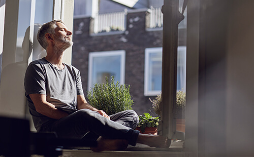 Ein Mann sitzt am offenen Fenster und genießt die Sonnenstrahlen.