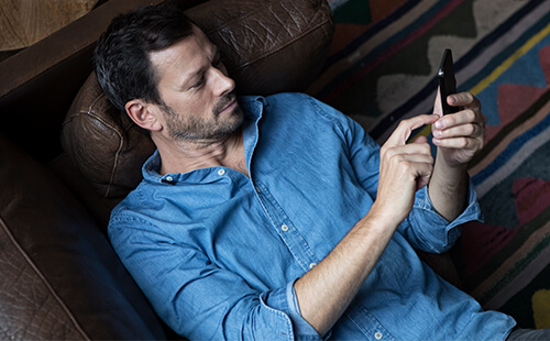 Ein Mann liegt auf der Couch und liest etwas an seinem Handy.