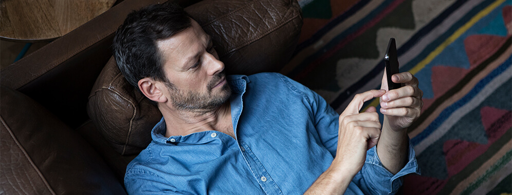 Ein Mann liegt auf der Couch und liest etwas auf seinem Handy.