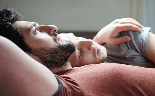 Zwei Männer liegen Arm in Arm im Bett.