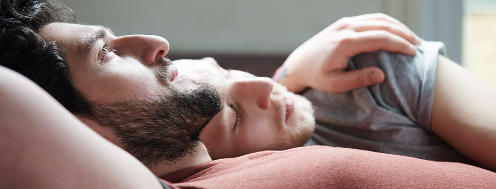 Zwei Männer liegen Arm in Arm im Bett.