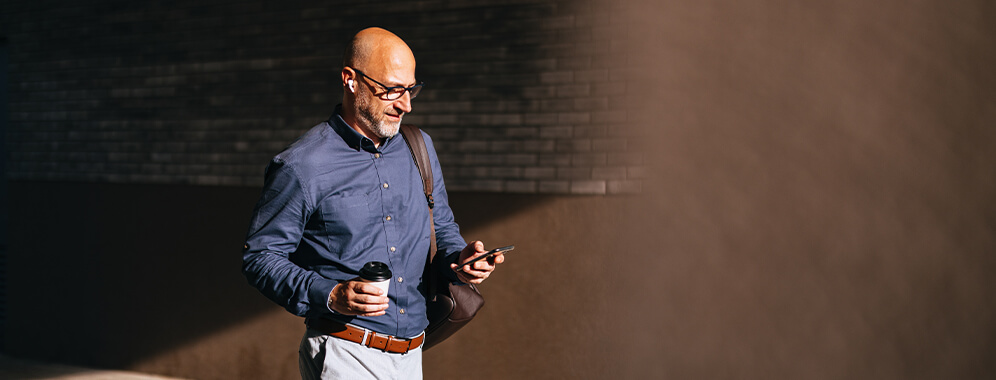 Ein Mann blickt gehend auf sein Handy. 
