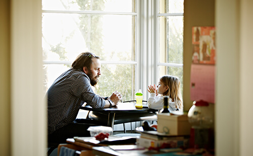 Ein Mann unterhält sich mit seinem kleinen Kind, sie sitzen am Tisch.