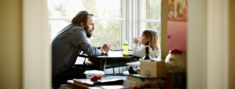 Ein Mann unterhält sich mit seinem kleinen Kind am Tisch sitzend.