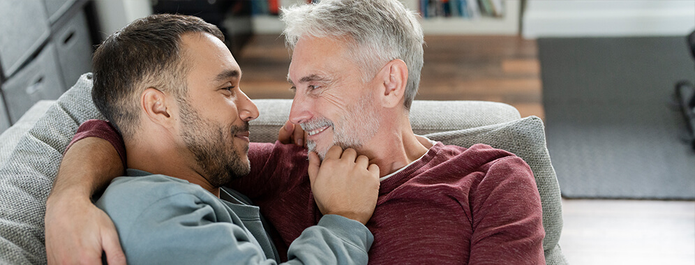 Zwei Männer liegen Arm in Arm auf dem Sofa. 
