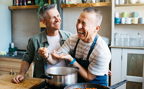 Zwei Männer lachen beim gemeinsamen Kochen.