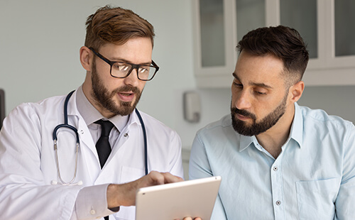 Ein Arzt erklärt einem Patienten etwas, beide schauen auf einen Bildschirm. 