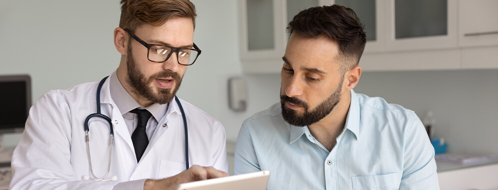 Ein Arzt erklärt einem Patienten etwas, beide schauen auf einen Bildschirm. 