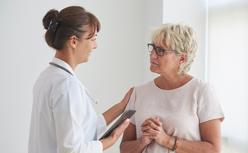 Eine Ärztin spricht mit einer MS-Patientin und legt ihr eine Hand auf die Schulter.