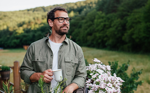 Ein Mann steht mit einer Tasse in der Hand im Garten. 