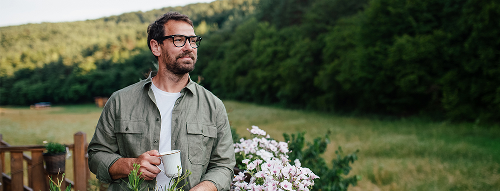 Ein Mann steht im Garten, er hält eine Tasse in der Hand. 