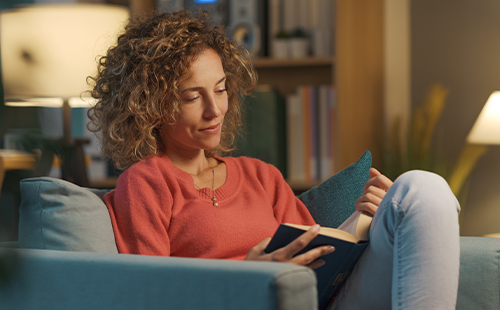 Eine Frau sitzt auf dem Sofa und liest ein Buch über die Geschichte von MS.