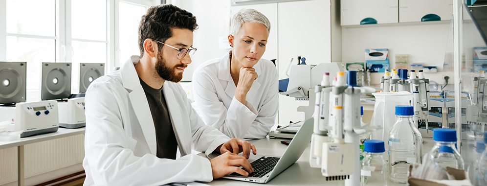 Ein Mann und eine Frau stehen in einem Labor am Laptop und arbeiten.