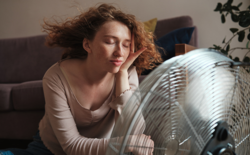 Eine Frau mit MS sitzt vor einem Ventilator und kühlt sich ab.