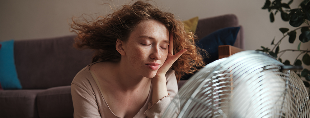 Eine junge Frau mit MS sitzt vor einem Ventilator und kühlt sich ab. 