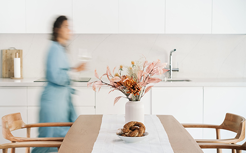 Man sieht ein gemütliches Zuhause im Skandi-Look. Im Hintergrund geht eine Frau mit MS, man sieht sie nur verschwommen. 