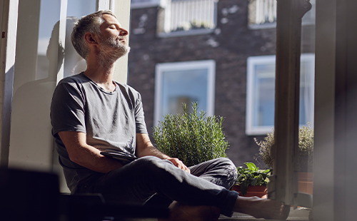 Ein Mann sitzt auf einer Fensterbank und lässt sich die Sonne ins Gesicht scheinen. 