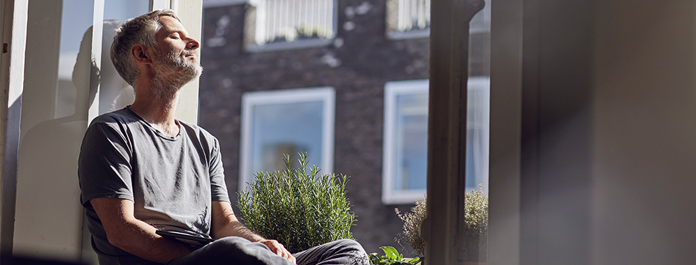 Ein Mann sitzt auf einer Fensterbank und lässt sich die Sonne ins Gesicht scheinen.