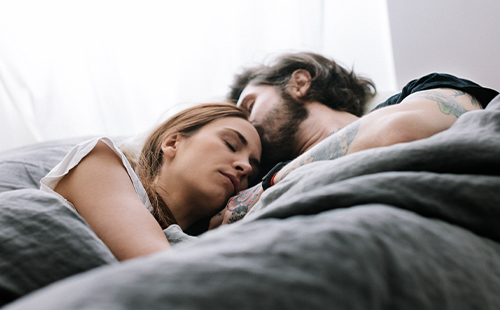 Eine Frau mit MS liegt schlafend im Bett neben ihrem Partner.
