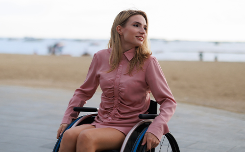 Eine junge Frau mit MS sitzt im Rollstuhl am Strand. 