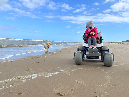 Bloggerin Anna Berkel im Strandrollstuhl mit ihrem Hund am Strand. 