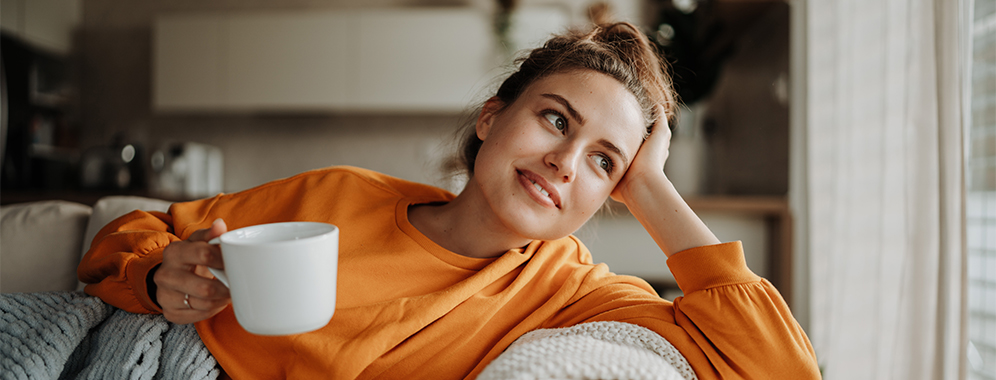 Frau sitzt mit Tasse auf der Couch.