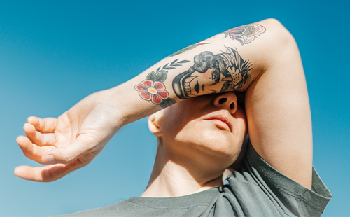 Eine junge Frau mit MS hält ihren tätowierten Arm vors Gesicht. 