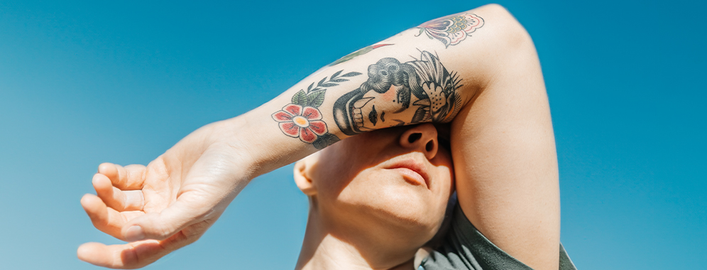 Eine junge Frau mit MS hält ihren tätowierten Arm vors Gesicht, die Sonne scheint darauf.