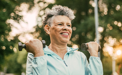 Ältere Dame mit MS macht HIT-Training mit Hanteln im Freien. 