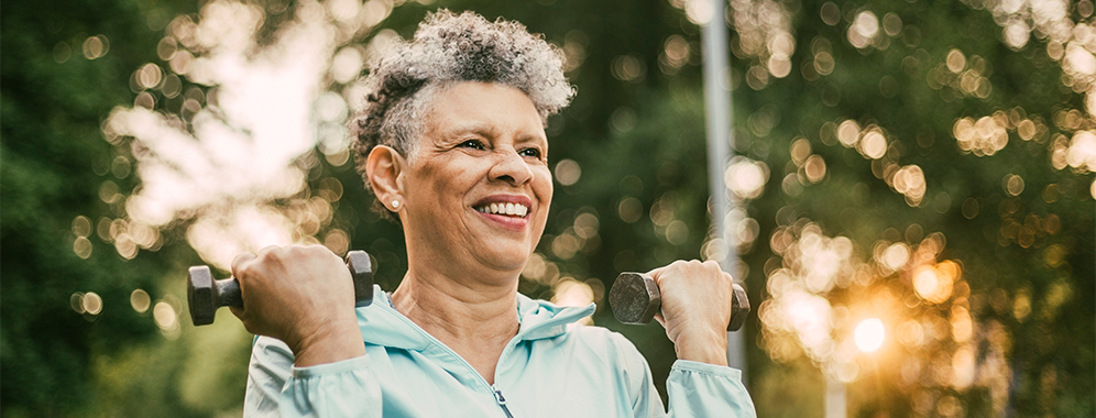 Ältere Dame mit MS beim HIT-Training mit Hanteln im Freien. 