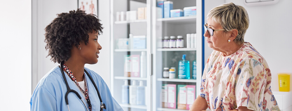 Man sieht eine ältere Frau im Gespräch mit einer Ärztin in der Arztpraxis. 