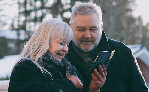 Ein Paar guckt vergnügt auf das Handy, während sie draußen spazieren gehen. 