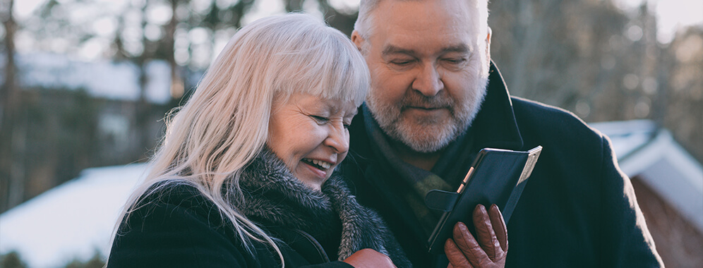 Ein älteres Pärchen schaut sich lächelnd etwas auf dem Mobiltelefon an. 