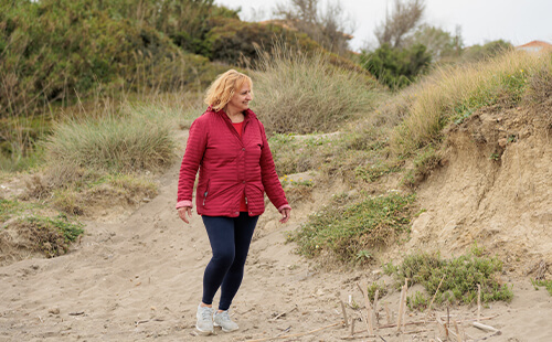 Eine Frau in roter Jacke geht in den Dünen spazieren. 