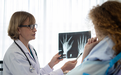 Eine Ärztin zeigt der Patientin Röntgenbilder einer Hand. 