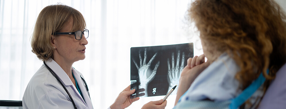 Eine Ärztin zeigt der Patientin Röntgenbilder einer Hand.
