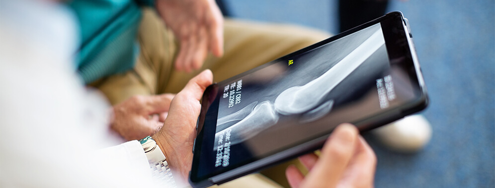Personen schauen sich ein Röntgenbild von Knochen auf dem Tablet an. 
